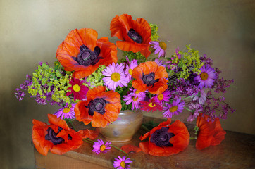 Bouquet of red poppies and different wild flowers in a basket isolated on a green-brown background
