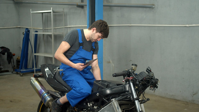 Technician sits on motorcycle and looks at tablet