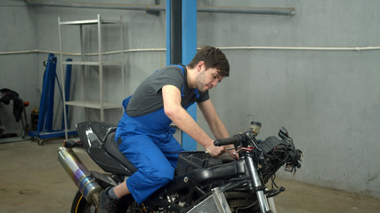 Fototapeta na wymiar Slow motion, technician sits on motorcycle and repairs it