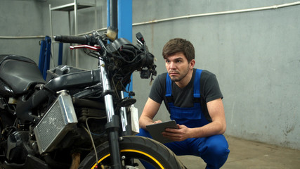 Fototapeta na wymiar Mechanic with tablet tries to repair a motorcycle in car service