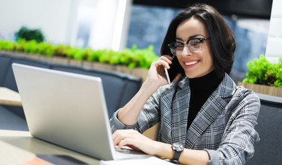 Climbing the career ladder. Close-up photo of a young female office worker talking on the phone with clients and working on her laptop.