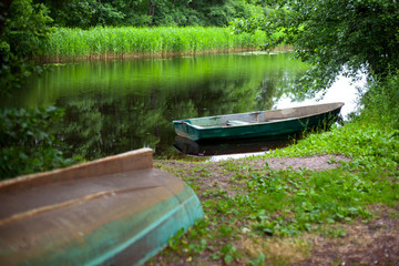 Boat on the Bank of a calm river, reflections of green trees