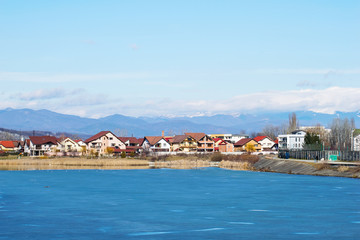 A village on the edge of a frozen lake, near the mountains.