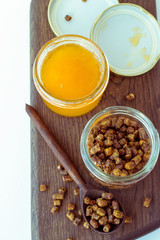 Beekeeping products. Propolis bee pollen and a jar of fresh honey on a wooden board against a light background. Toned photo.