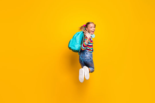Full body back rear spine photo energetic schoolchild jump wave hand greet schoolmates wear blue bag rucksack striped sweater denim jeans gumshoes isolated bright shine yellow color background