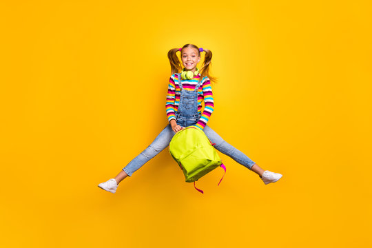 Full size photo cheerful schoolchild jump wear headset striped sweater jeans denim bag rucksack enjoy primary school lesson isolated over bright shine yellow color background