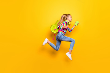 Fototapeta na wymiar Full size profile side photo kid jump run runner hurry fast lesson hold smartphone headset backpack striped suspenders overalls sweater denim jeans isolated bright shine yellow color background