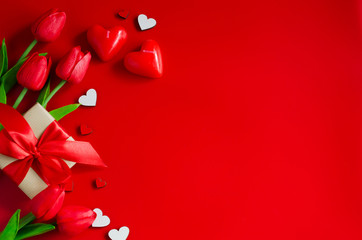 Red tulips, gift boxes and wooden hearts on red background. Greeting card for Valentine's Day.