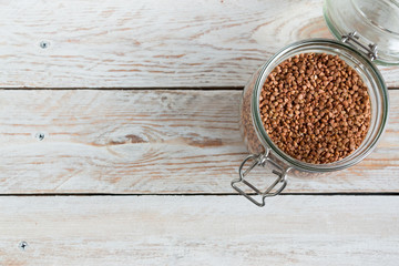 Buckwheat groats in a glass jar on a wooden table on a light background. Close-up. The concept of vegetarianism and a balanced diet.