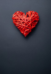 Red wicker heart made of twigs on a black background with place for text