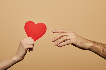 cropped view of woman holding red heart and man reaching it isolated on beige