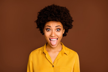 Fototapeta na wymiar Closeup photo of funny beautiful dark skin wavy lady positive good mood sticking tongue out of mouth fooling around wear yellow shirt blouse isolated brown color background
