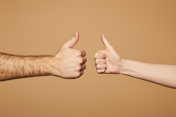 cropped view of man and woman showing thumbs up isolated on beige