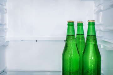 Three sweaty beer bottles on a shelf in an empty refrigerator. Copy space