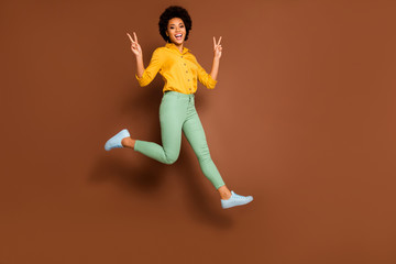 Fototapeta na wymiar Full length profile photo of funny dark skin lady jump high up go shopping showing v-sign symbols wear yellow shirt green pants footwear isolated brown color background