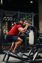 Athletic man doing legs exercise on squat machine at the gym