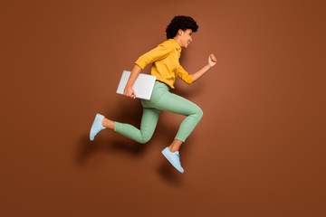 Fototapeta na wymiar Full length profile photo of funny dark skin lady jumping high holding notebook hurry classes lessons schoolgirl wear yellow shirt green trousers shoes isolated brown color background
