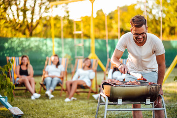 Friends having a barbecue party outdoors. Portrait of a handsome man cooking meat on a grill.