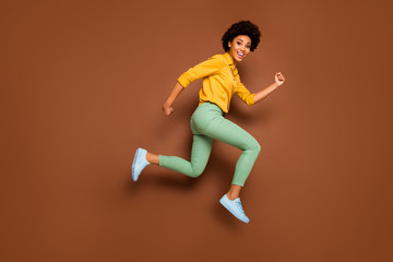 Fototapeta na wymiar Full body photo of funny dark skin wavy lady jumping up high rushing discount shopping center black friday wear yellow shirt green pants shoes isolated brown color background