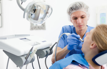 Professional dentist examining and performing treatment to young woman