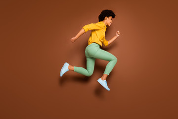 Fototapeta na wymiar Full length photo of funny dark skin lady jumping up high rushing discount shopping center black friday wear yellow shirt green pants footwear isolated brown color background