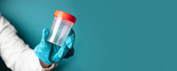 Doctor hand in latex blue glove holds a plastic container for testing on a blue background