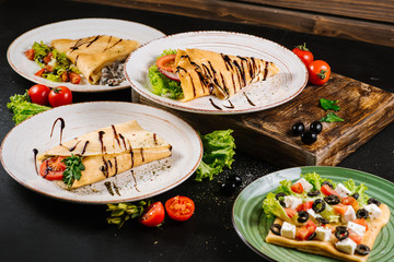 Thin pancakes with vegetables on black background