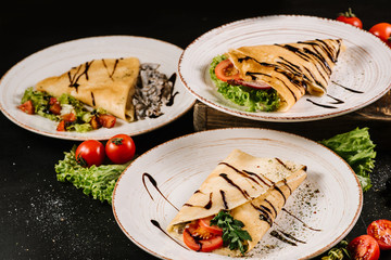 Thin pancakes with vegetables on black background