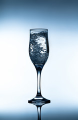 Glass of sparkling water with bubbles reflected on surface on which it stands. Closeup on white and blue gradient background