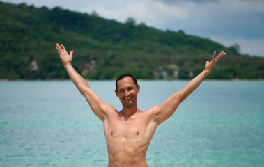 Portrait of a handsome happy man at tropical resort with smile and raised his arms up