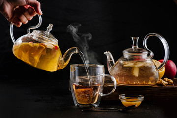 Glass teapots with fruit tea in composition on black background