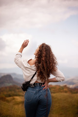 curly-haired woman looks at the mountains. reaching for the sky.