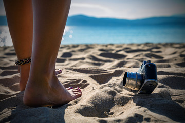 Retro analogue camera with woman's feet on the sand.