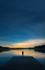 Silueta de mujer mirando el atardecer en el reflejo del lago