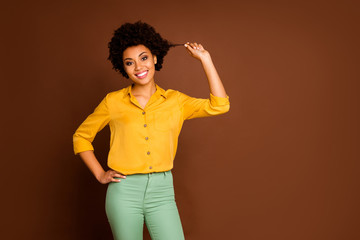 Photo of charming beautiful dark skin lady holding wavy curl showing nice results after visiting hair salon master wear yellow shirt green pants isolated brown color background