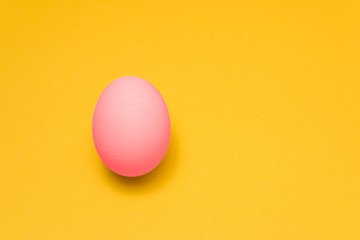 one easter egg painted in pastel pink color on a yellow background with copyspace. happy holiday
