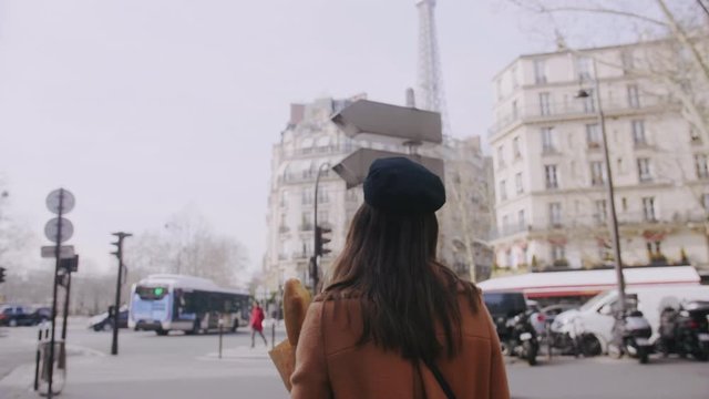 Camera follows beautiful happy food blogger woman walking along Paris street with shopping paper bag slow motion.