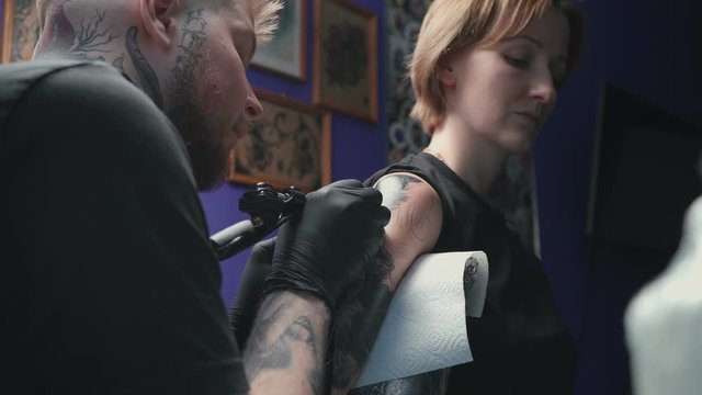 Video of man doing dark tattoo of snake for woman in studio