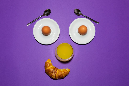 Fun breakfast concept with abstract smiling, happy human face made of breakfast items on purple background.