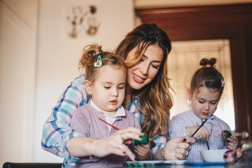 A mother with two female toddlers painting eggs for Easter.