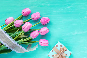 Pink tulips and gift in a box on a turquoise wooden table. Spring festive background, top view, flat lay, copy space.