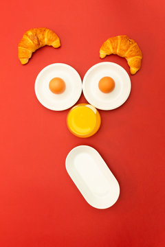Fun breakfast concept with abstract astonished human face made of breakfast items on red background.