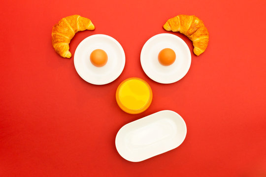 Fun breakfast concept with abstract smiling, happy human face made of breakfast items on red background.