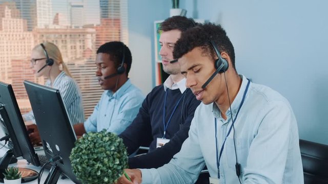 Medium shot of Frustrated and angry mixed-race call center agent talking to the client on phone. Then he breaking his pencil in half and throwing away.
