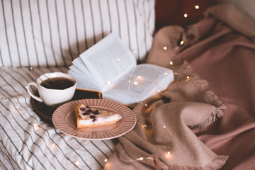 Tasty fruit pie with fresh black tea and open book on wooden tray with glowing lights closeup. Good morning. Breakfast time.