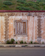 Exterior of aged house with weathered ornamental walls and shuttered window located under green...