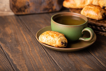 Green cup of tea with mini chocolate bun, puff pastry on old wooden table. Tasty tea break concept, copy space.