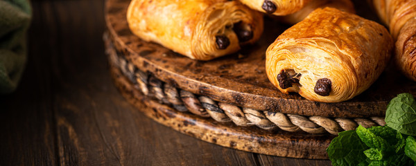 Obraz premium Freshly baked sweet buns puff pastry with chocolate and croissants on old wooden background. Breakfast or brunch concept with copy space, banner.