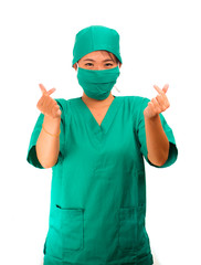 young beautiful and happy Asian woman medicine doctor or chief hospital nurse in green scrubs and surgeon hat smiling confident doing love finger sign