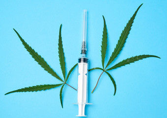 plastic syringe with a needle and green leaves of hemp